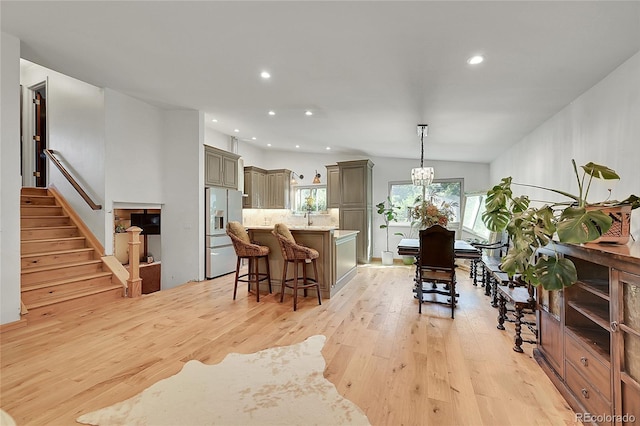 kitchen with light hardwood / wood-style floors, light stone countertops, pendant lighting, white fridge with ice dispenser, and a notable chandelier