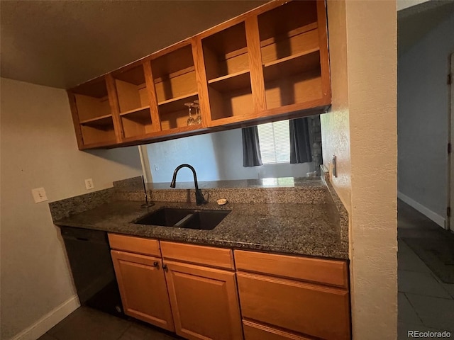 kitchen featuring a sink, baseboards, dark tile patterned floors, black dishwasher, and dark stone counters