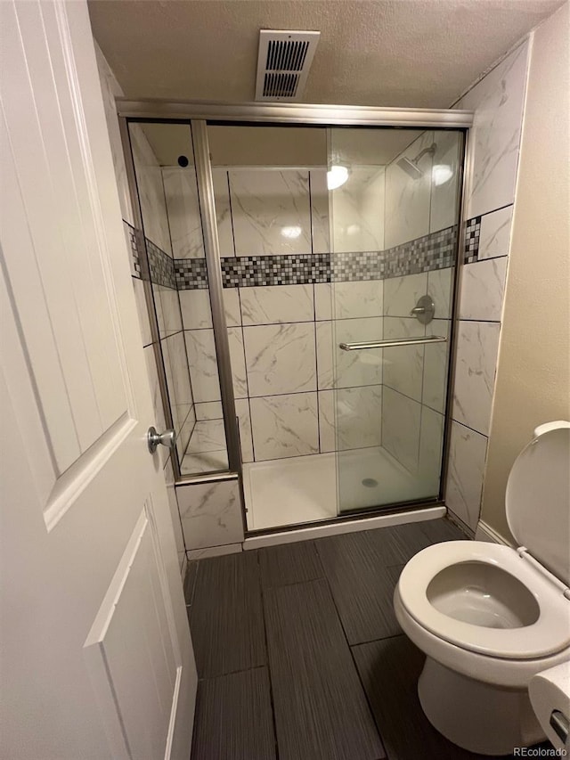 bathroom with toilet, a stall shower, and a textured ceiling