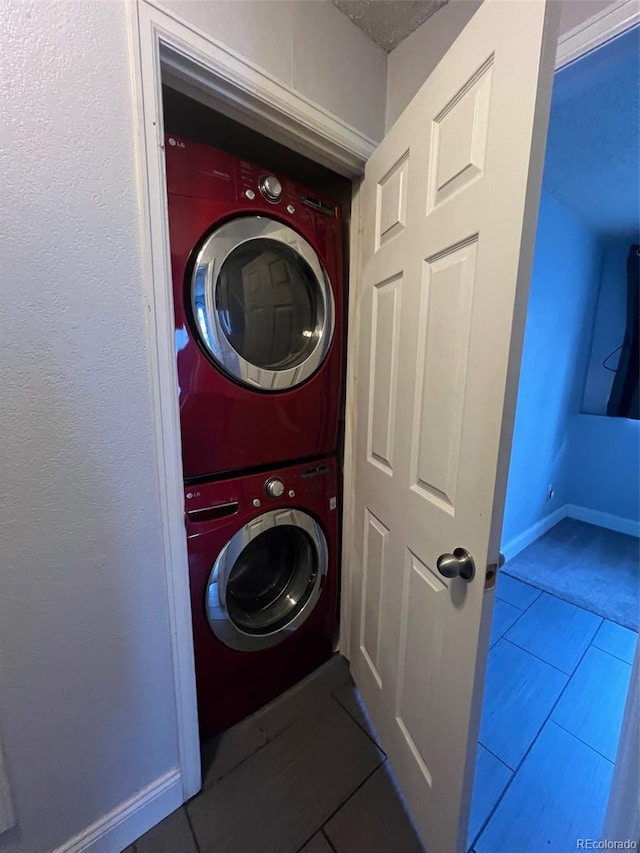 laundry area with stacked washer / drying machine, tile patterned floors, and baseboards