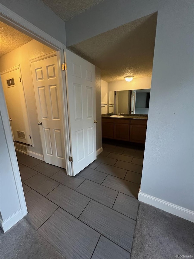 hall with a textured ceiling, baseboards, a sink, and dark tile patterned flooring