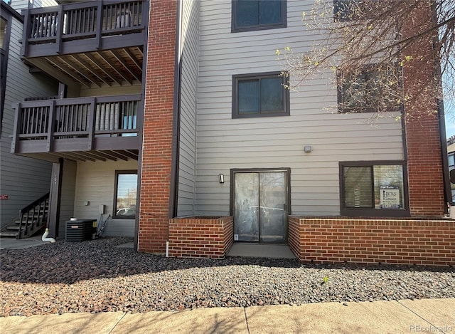 back of house featuring brick siding, a balcony, stairway, and cooling unit