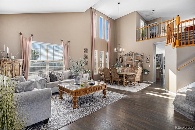 living area with stairway, wood finished floors, baseboards, a towering ceiling, and a chandelier