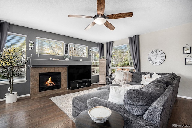 living room featuring a tiled fireplace, a textured ceiling, baseboards, and wood finished floors