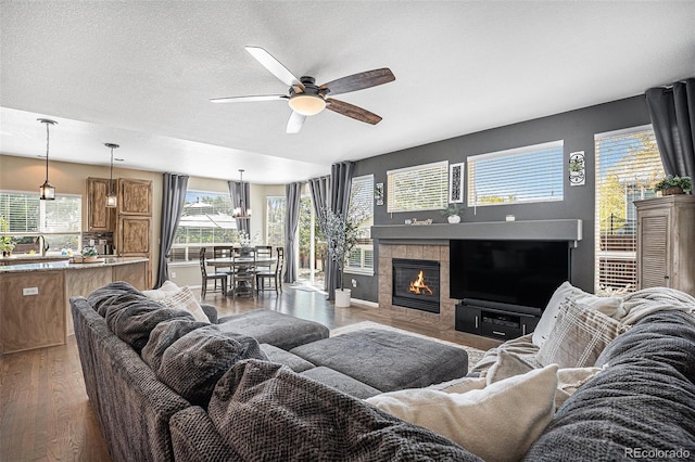 living area featuring a fireplace, a textured ceiling, a ceiling fan, and wood finished floors