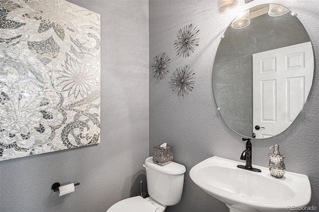 half bath featuring toilet, a textured wall, and a sink