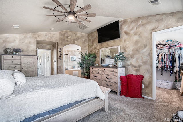 carpeted bedroom with arched walkways, visible vents, a walk in closet, and vaulted ceiling