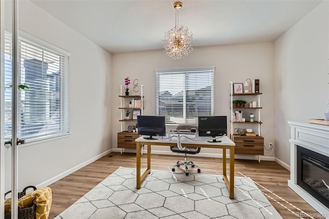 office area with a glass covered fireplace, a notable chandelier, baseboards, and light wood-type flooring