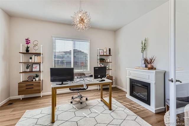 office area featuring a chandelier, a glass covered fireplace, baseboards, and wood finished floors