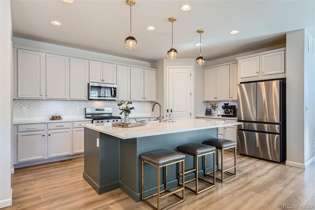 kitchen featuring a breakfast bar area, light wood finished floors, a sink, light countertops, and appliances with stainless steel finishes