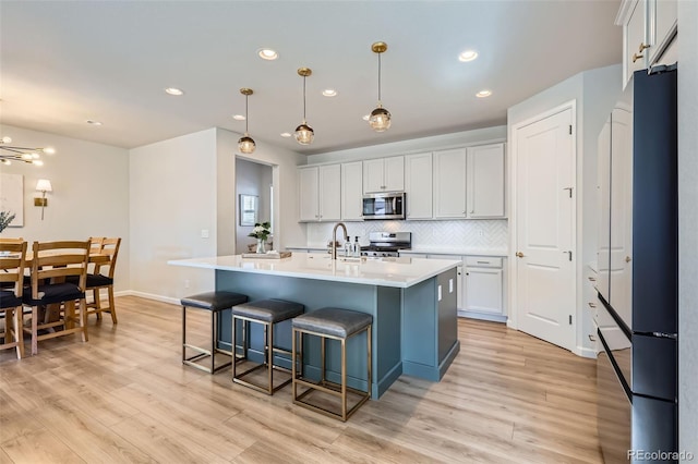 kitchen featuring backsplash, light countertops, light wood-style flooring, a kitchen breakfast bar, and stainless steel appliances