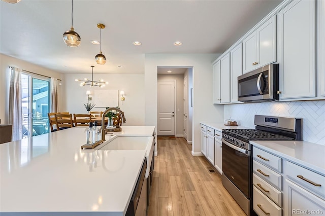 kitchen with light wood-type flooring, a sink, backsplash, appliances with stainless steel finishes, and light countertops