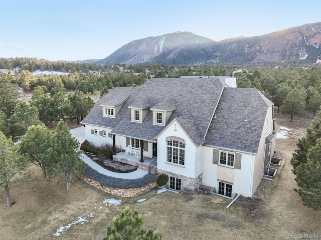 view of front of property with a shingled roof, a patio, a chimney, a mountain view, and stucco siding