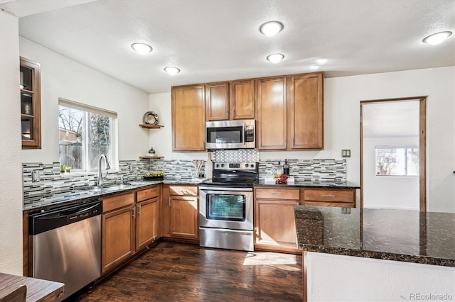 kitchen with dark wood-type flooring, a sink, appliances with stainless steel finishes, dark stone counters, and tasteful backsplash