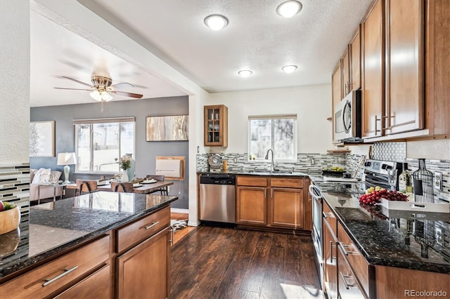 kitchen with dark wood-style floors, appliances with stainless steel finishes, brown cabinets, dark stone countertops, and a sink