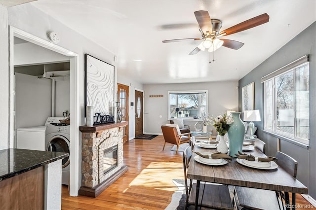 dining space featuring a fireplace, light wood-style floors, ceiling fan, washer and dryer, and baseboards