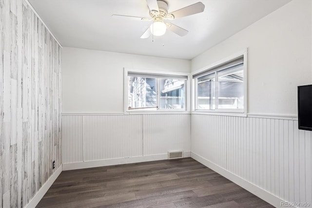 unfurnished room with ceiling fan, visible vents, wood finished floors, and wainscoting