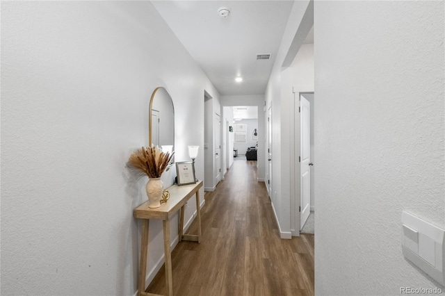 hallway with visible vents, baseboards, and wood finished floors