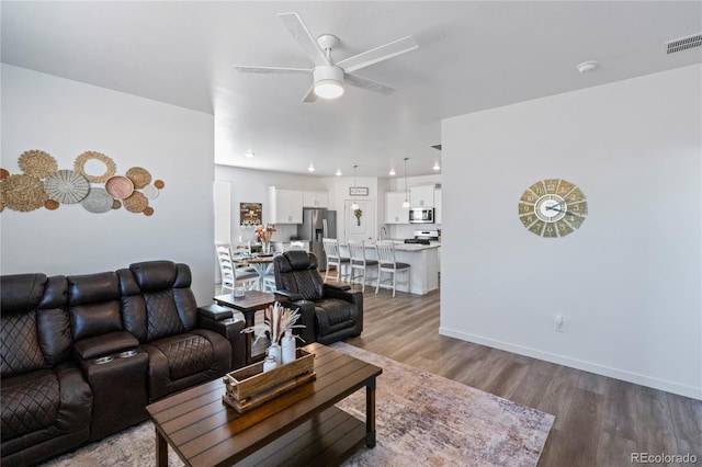 living room with baseboards, wood finished floors, visible vents, and a ceiling fan