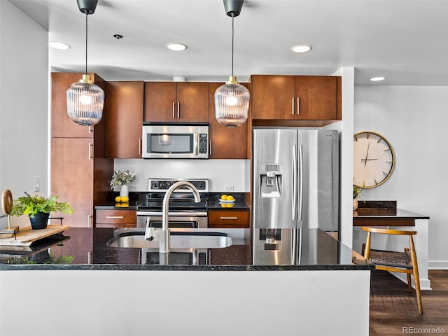 kitchen featuring appliances with stainless steel finishes, decorative light fixtures, dark stone counters, and dark hardwood / wood-style flooring