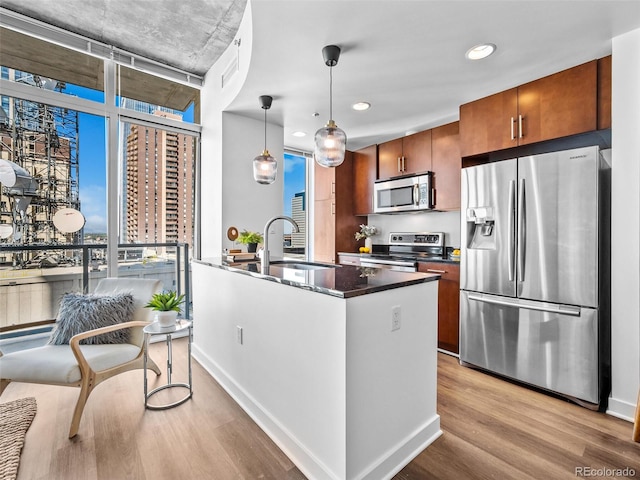 kitchen featuring sink, light wood-type flooring, an island with sink, hanging light fixtures, and stainless steel appliances