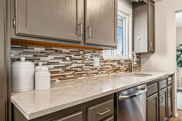 kitchen featuring tasteful backsplash, dishwasher, light stone countertops, and a sink