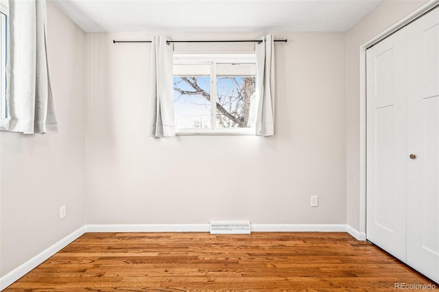 unfurnished bedroom with a closet, visible vents, baseboards, and wood finished floors