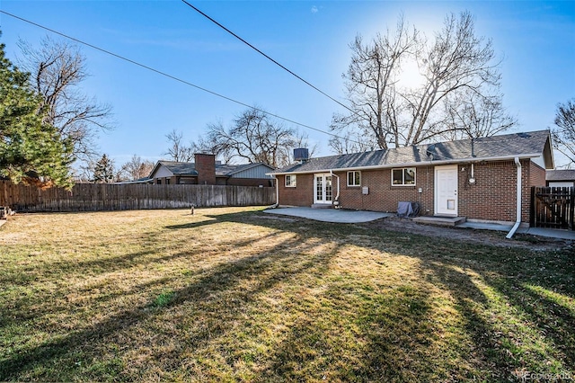 rear view of property with a lawn, a fenced backyard, brick siding, a chimney, and a patio area