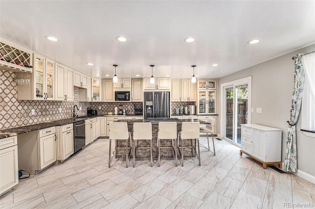 kitchen featuring cream cabinets, a breakfast bar area, decorative light fixtures, and black appliances