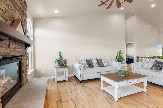 living room with ceiling fan, high vaulted ceiling, light hardwood / wood-style flooring, and a stone fireplace