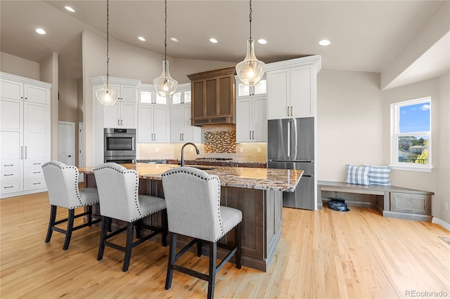 kitchen featuring a kitchen island with sink, dark stone countertops, a kitchen bar, light wood-type flooring, and appliances with stainless steel finishes