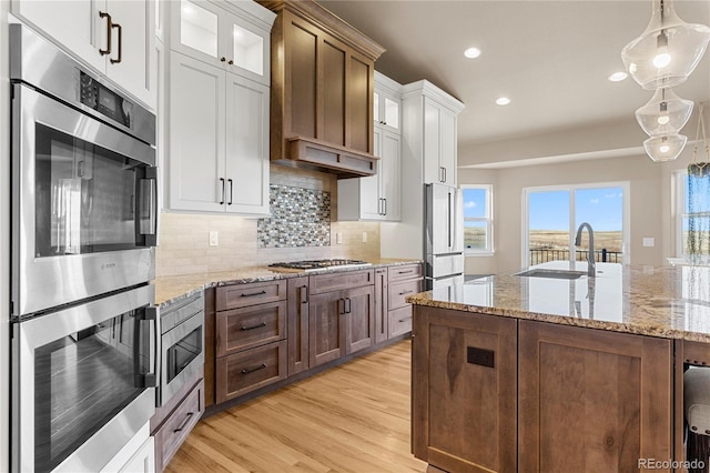 kitchen with white cabinetry, decorative light fixtures, stainless steel appliances, and light wood-type flooring