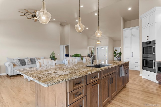 kitchen featuring a center island with sink, sink, white cabinetry, and light hardwood / wood-style flooring