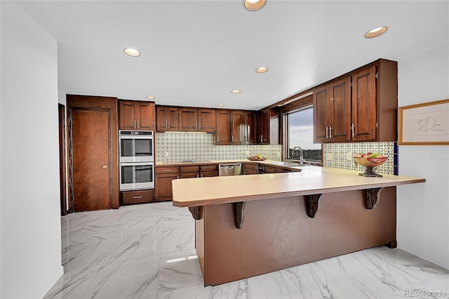 kitchen with marble finish floor, light countertops, decorative backsplash, appliances with stainless steel finishes, and a peninsula