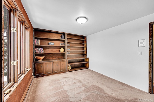 spare room featuring built in shelves, a baseboard radiator, and light colored carpet