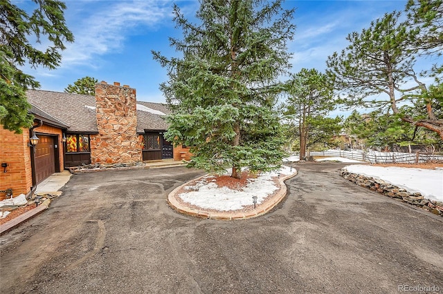 view of front of home with a chimney, a shingled roof, fence, a garage, and driveway