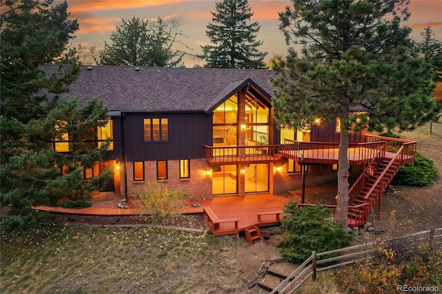 back of house featuring stairway, brick siding, a shingled roof, and a deck