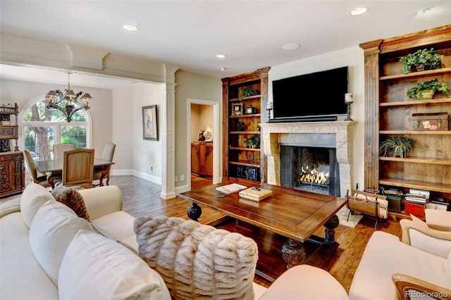 living room featuring a notable chandelier, built in features, decorative columns, and wood-type flooring