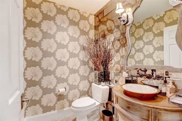 bathroom with baseboards, vanity, toilet, and wallpapered walls