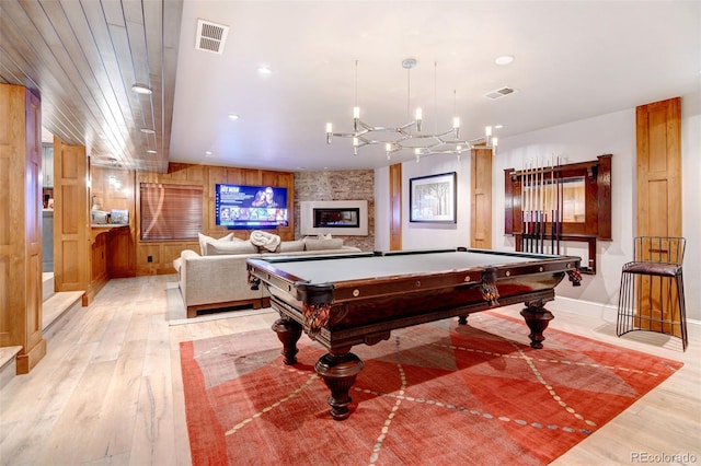 game room featuring pool table, light wood-type flooring, wooden walls, and a stone fireplace