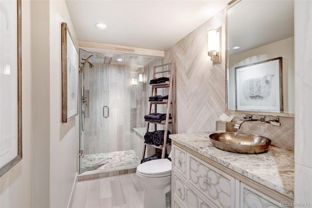 bathroom featuring a shower with door, vanity, and toilet