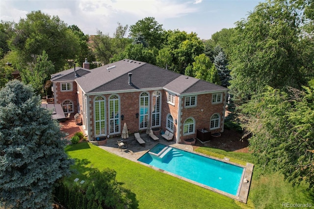 rear view of house with brick siding, a lawn, a chimney, and an outdoor pool