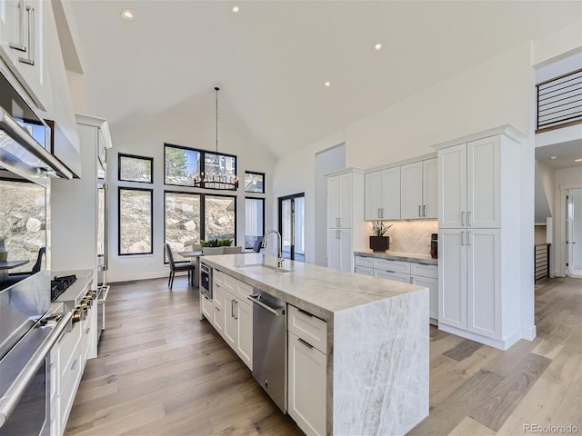 kitchen featuring tasteful backsplash, light wood-type flooring, white cabinets, and an island with sink