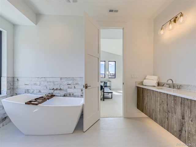 bathroom with a bath to relax in, tile floors, tile walls, and lofted ceiling