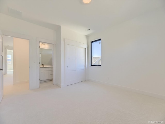 unfurnished bedroom with light carpet, a closet, and ensuite bathroom