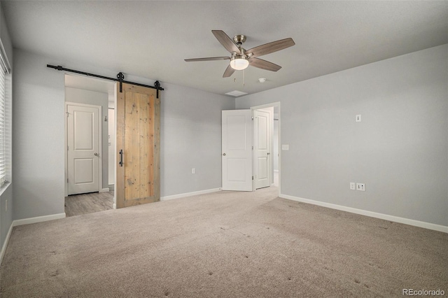 unfurnished bedroom featuring ceiling fan, a barn door, and light colored carpet