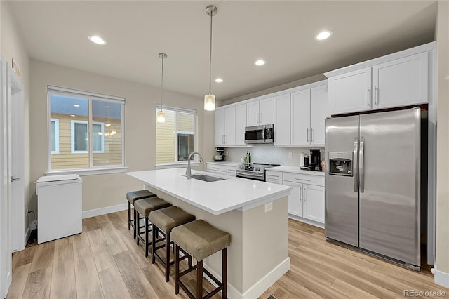 6745 S Tempe Ct, Aurora, CO 80016 - kitchen featuring appliances with stainless steel finishes, an island with sink, light wood finished floors, white cabinets, and backsplash