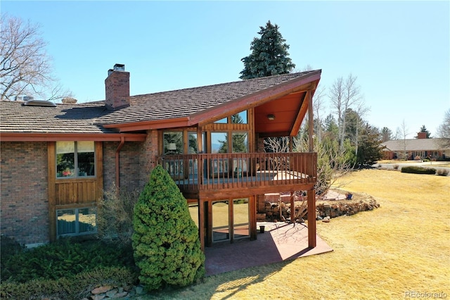 rear view of property featuring a wooden deck, a lawn, a chimney, and a patio area