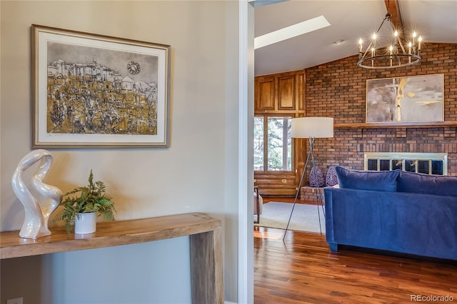 living area featuring a brick fireplace, vaulted ceiling with skylight, an inviting chandelier, and wood finished floors