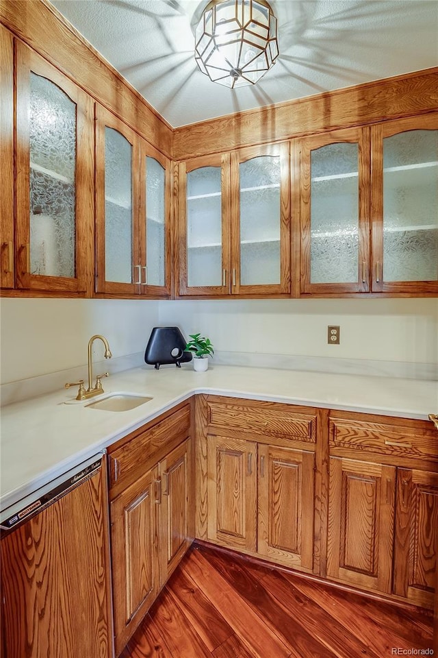 kitchen featuring glass insert cabinets, light countertops, dishwashing machine, dark wood-style floors, and a sink